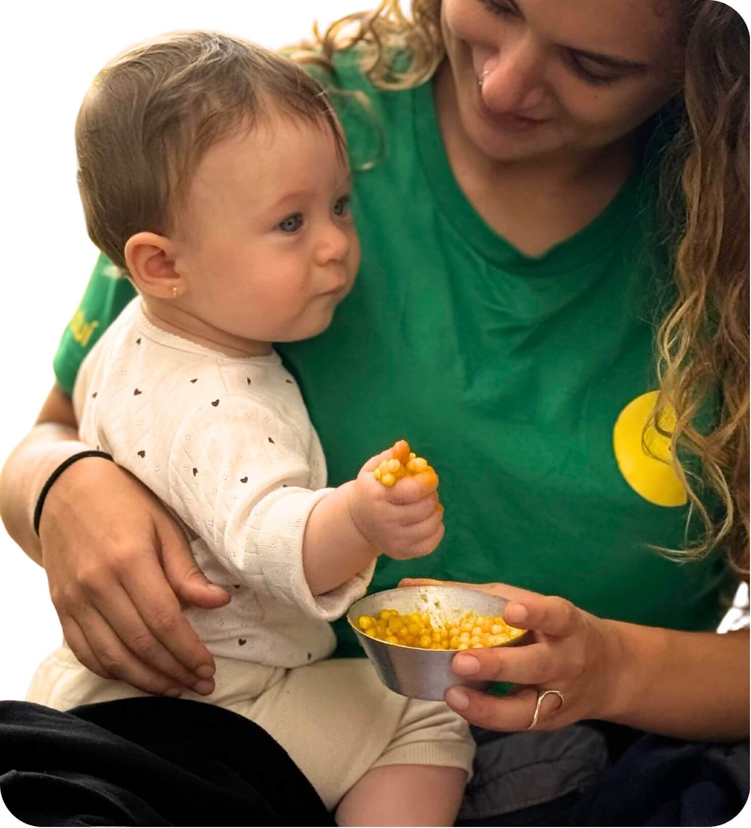Educadora sorrindo para um bebê que segura milho no colo